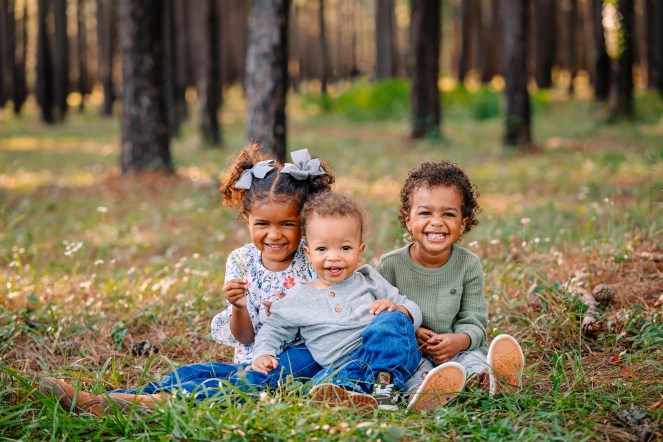 Three happy siblings smiling among fall foliage in a forest
